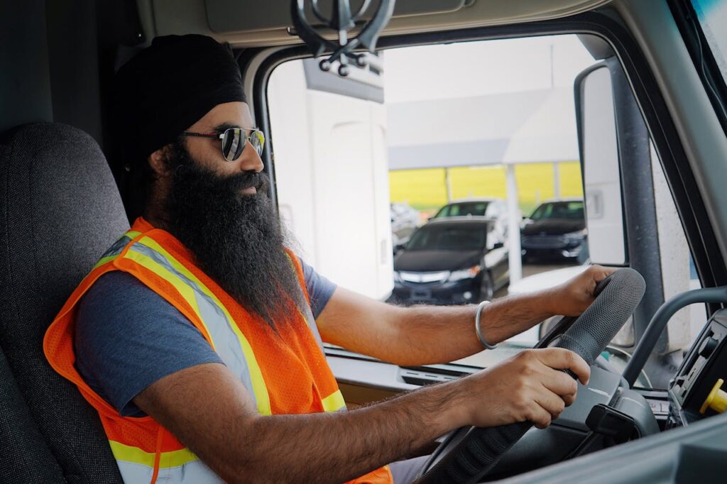 14797995 Bearded truck driver wearing a turban and safety vest inside a truck cab, focused on driving.